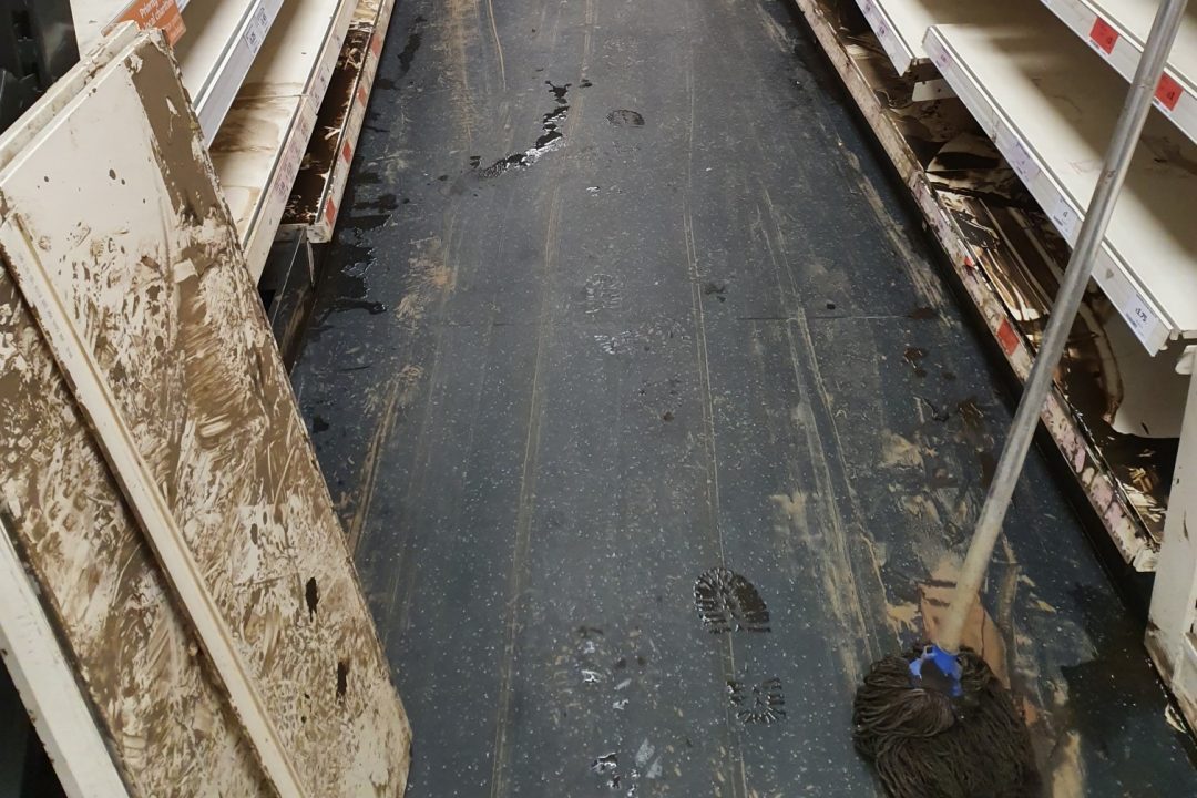 The inside of a shop after flooding, with mud across the floor and stripped shelving
