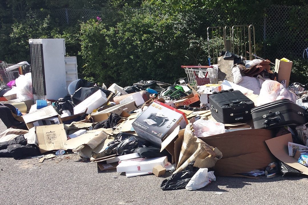 A large pile of fly-tipped waste, including a fridge, suitcases and cardboard, dumped on tarmac
