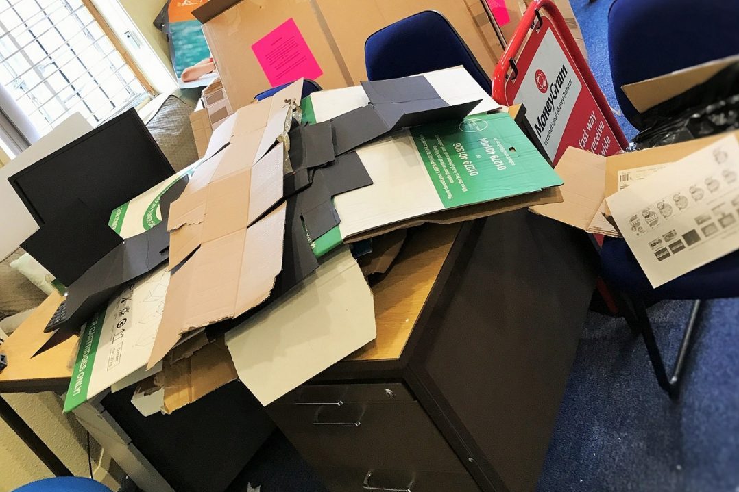 Flattened cardboard packaging stacked on office desks and filing cabinets during a clear out