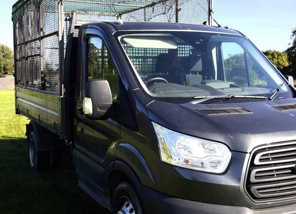 A caged tipper vehicle parked on grass, ready for a collection